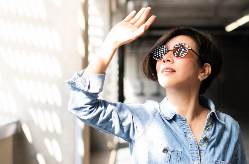 Woman using her hand to protect herself from sun glare that comes through the blinds.