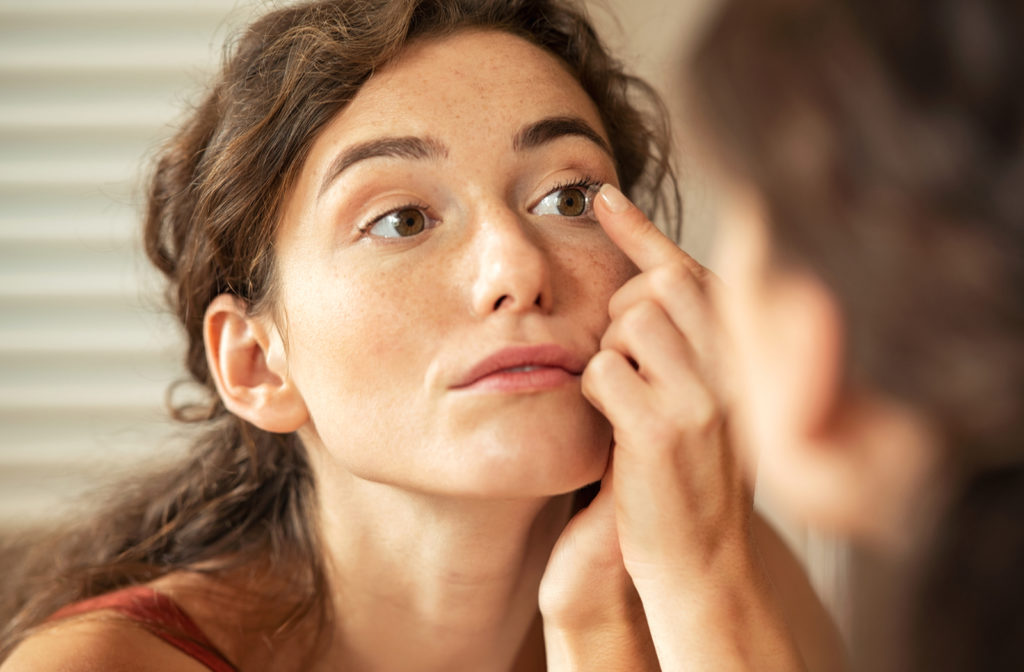 Young woman trying on contact lenses as she looks at self in mirror.