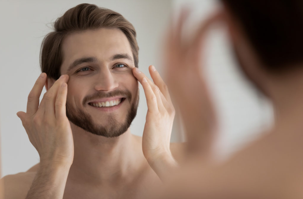 Man looking in mirror touching eyes satisfied with results after wearing eye mask during sleep
